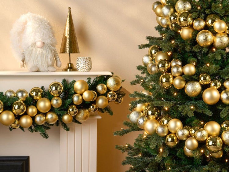 Weihnachtsbaum geschmückt mit glänzenden und matten goldenen Kugeln und Lichterkette, Kamin mit Tannengirlande und weihnachtlicher Dekoration.