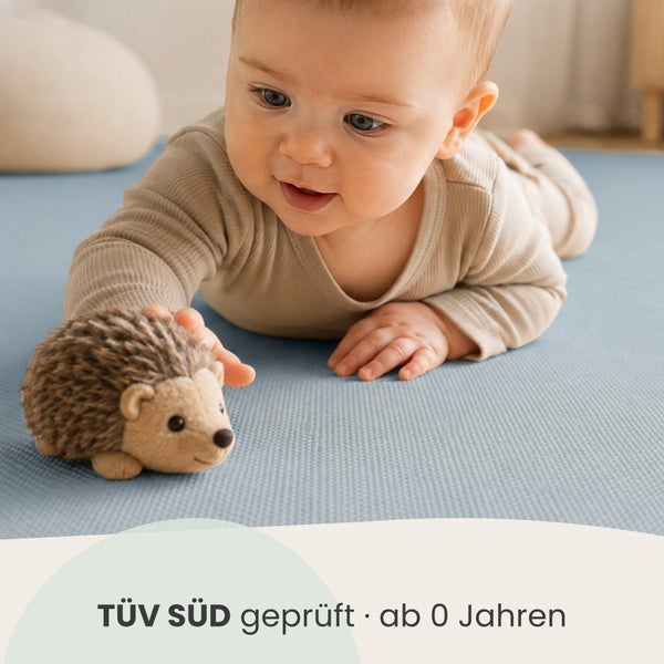Baby spielt auf einer Matte mit einem Igel Stofftier, TÜV SÜD geprüft für Kinder ab null Jahren.
