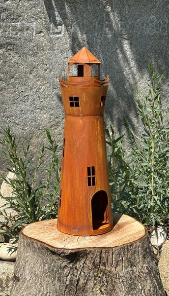 Dekorative Gartenleuchte in Leuchtturm Optik aus Metall mit Edelrostpatina auf einem Baumstumpf platziert.