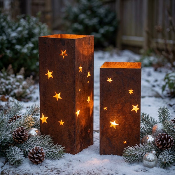 Zwei rechteckige Windlichter aus Metall mit Rostoptik und Sternenmotiven, platziert im Schnee mit Tannenzweigen und Weihnachtskugeln.