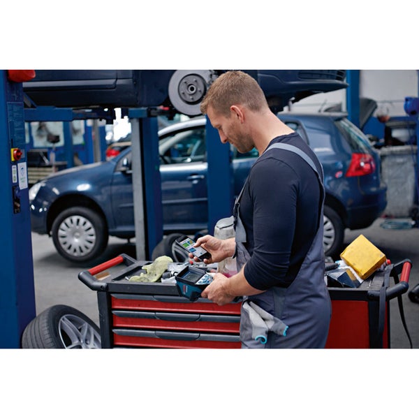 Ein Mechaniker verwendet ein Smartphone und ein Diagnosegerät in einer Werkstatt.