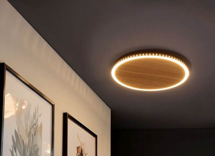 Runde LED-Deckenleuchte im Holzdesign mit leuchtendem Ring an einer dunklen Zimmerdecke montiert.