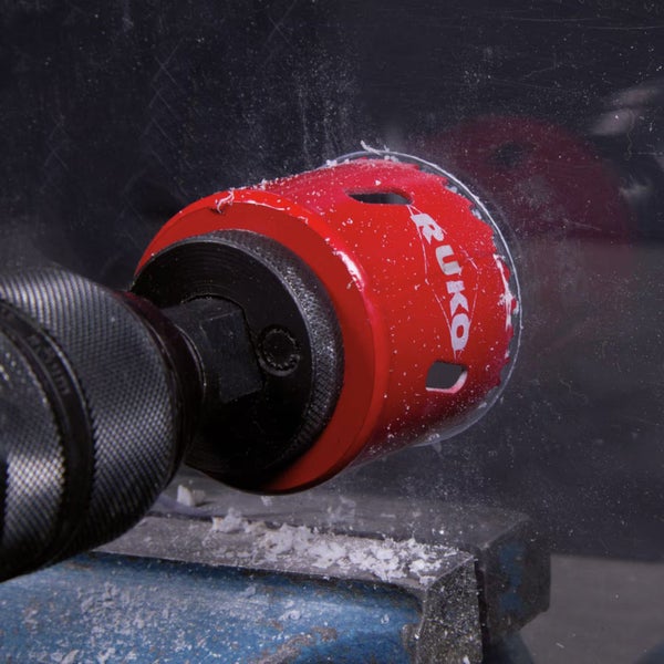 RUKO Lochsäge bohrt ein Loch in transparenten Kunststoff, weiße Späne sichtbar.