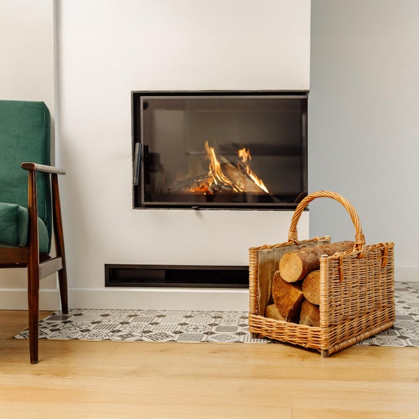 Modernes Wohnzimmer mit Einbaukamin und gefülltem Kaminholzkorb aus Weide auf gemusterten Bodenfliesen.
