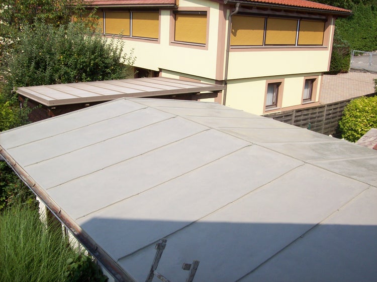 Flachdach mit grauer Abdichtung und Dachbahn neben einem Wohnhaus im Garten.