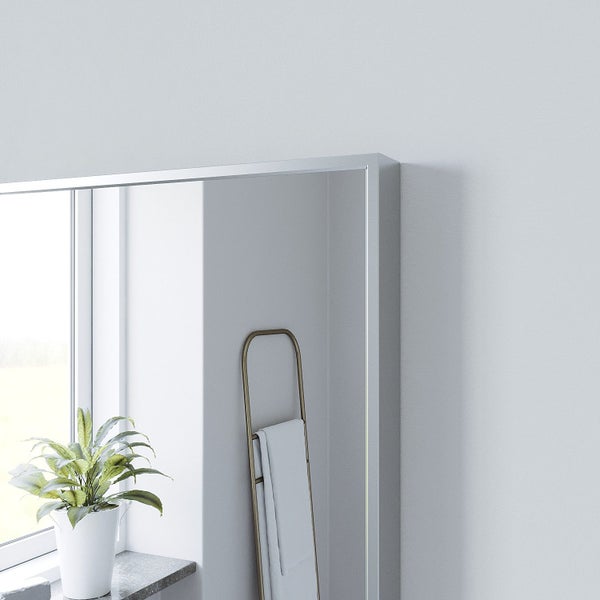 Ein moderner Wandspiegel mit minimalistischem Rahmen, platziert in einem hellen, aufgeräumten Wohnbereich neben einem Handtuchhalter.