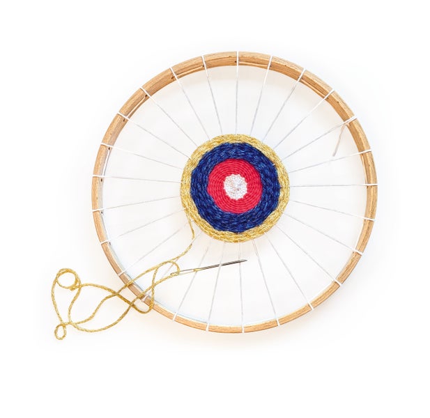 Stickrahmen aus Holz mit eingearbeitetem Garnmotiv in Zielscheibenoptik und einer beiliegenden Handarbeitsnadel mit Garnrest.