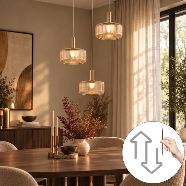Drei moderne Pendelleuchten mit geriffeltem Glas und höhenverstellbarer Funktion über einem Esstisch in einem hellen Wohnraum.