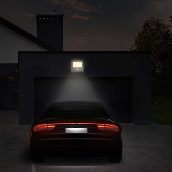 Szene mit einem LED-Strahler an einer Garagenwand, der ein geparktes Auto beleuchtet
