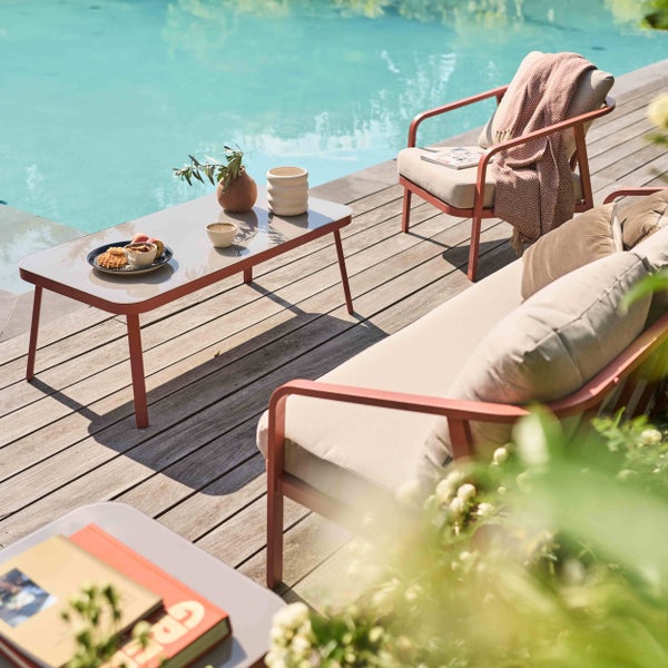 Moderne Gartenlounge auf einer Holzterrasse am Pool mit Couchtisch, Sessel und Sofa inklusive Polstern.