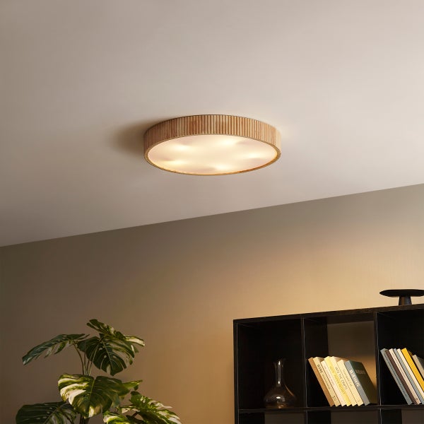 Runde Deckenleuchte mit Holzumrandung in Lamellenoptik, montiert in einem modern eingerichteten Raum mit Regal und Zimmerpflanze.
