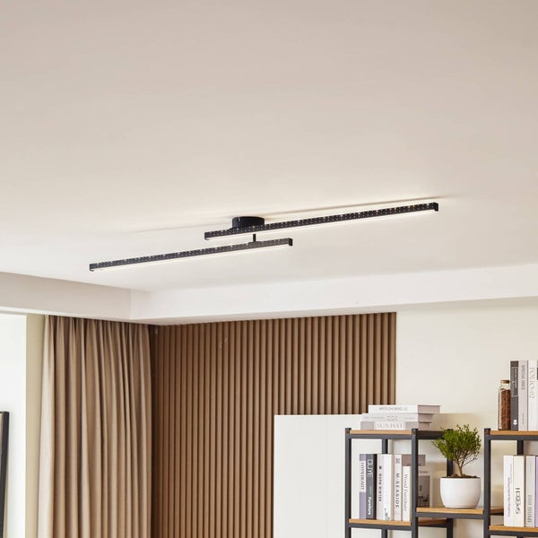 Moderne schwarze LED-Deckenleuchte mit zwei versetzten linearen Stäben und Lochmuster in einem hellen Raum mit Holzpaneelwand.