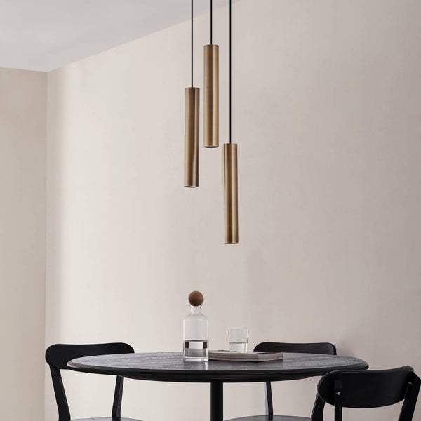 Drei Pendelleuchten aus Metall über einem Esstisch.