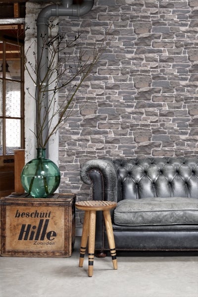 Dekoratives Zimmer mit Steinwand, Ledersofa und Holzhocker