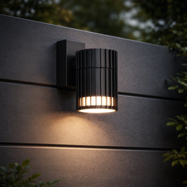 Moderne schwarze Außenwandleuchte in Zylinderform mit Lamellenstruktur und warmem Lichtschein nach unten.
