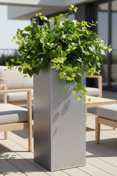 Hoher quadratischer Pflanzkübel in Grau mit grünen Pflanzen auf einer hellen Holzterrasse mit modernen Gartenmöbeln.