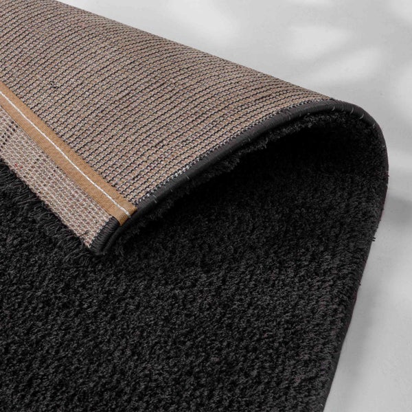 Dunkler Hochflor-Teppich mit weicher Textur und gewebter Rückseite, Detailansicht der Kante.