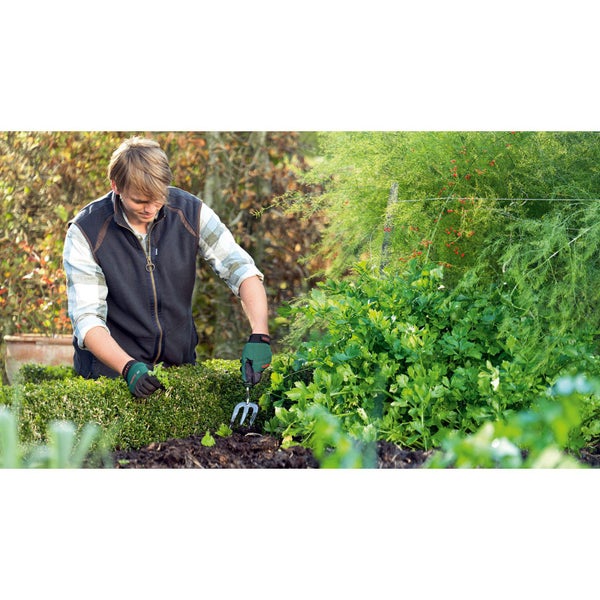 Person, die im Garten arbeitet, mit einer Harke neben einer Hecke und Pflanzen