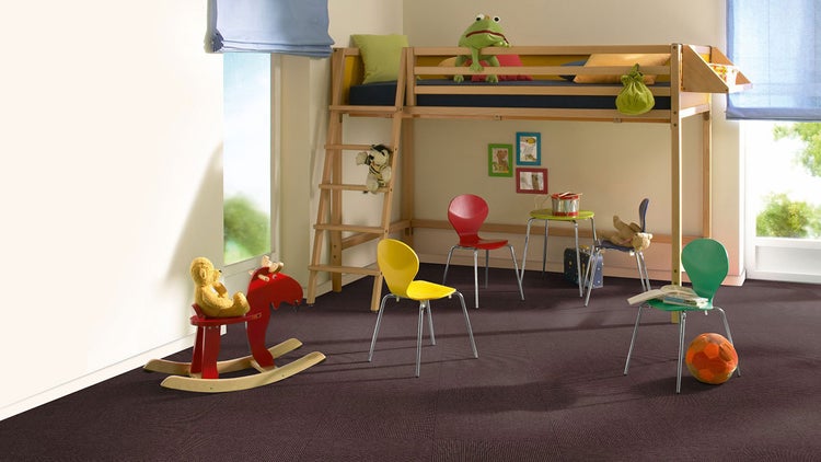 Helles Kinderzimmer mit dunklen Teppichfliesen, einem Etagenbett aus Holz mit Leiter und bunten Stühlen.