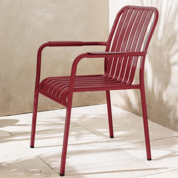 Roter Gartenstuhl aus Metall mit Armlehnen und Lamellendesign auf einer hellen Terrasse mit Steinboden.