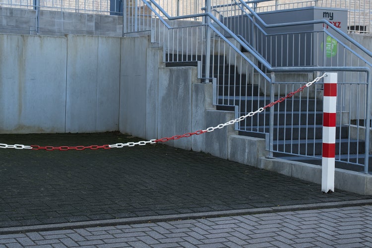 Kunststoff-Absperrkette rot-weiß an einem Absperrpfosten vor einer Außentreppe aus Beton mit Metallgeländer.