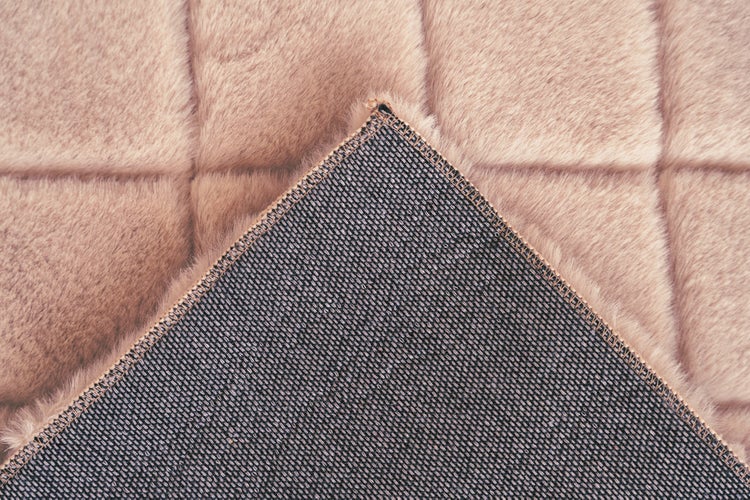 Nahaufnahme eines Kunstfellteppichs mit quadratischem Steppmuster und gewebter Rückseite.