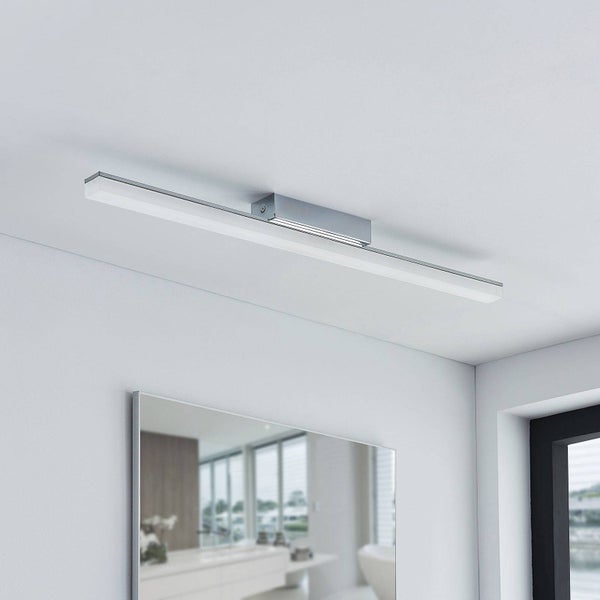 Moderne, lineare LED-Badezimmerwandleuchte aus Metall und Kunststoff, montiert über einem Spiegel in einem hellen, organisierten Badezimmer.