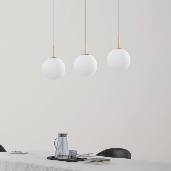 Dreiflammige Pendelleuchte mit weißen Glaskugeln und messingfarbenen Halterungen über einem gedeckten Esstisch.