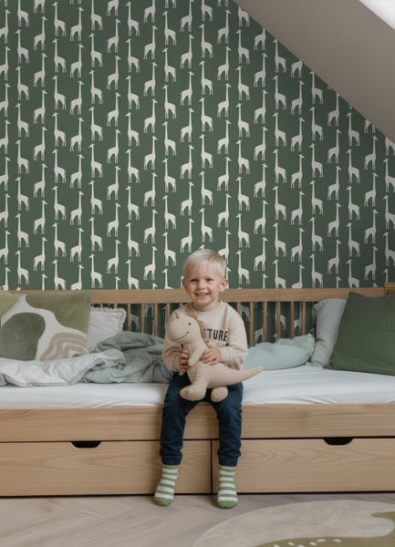 Kinderzimmer mit Vliestapete mit Giraffen-Muster auf grünem Hintergrund, Holzbett und hellen Textilien unter einer Dachschräge.