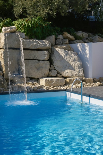 Außenpool mit einem Wasserfall über Natursteinen und einem gebogenen Wasserfallschwall aus Edelstahl.