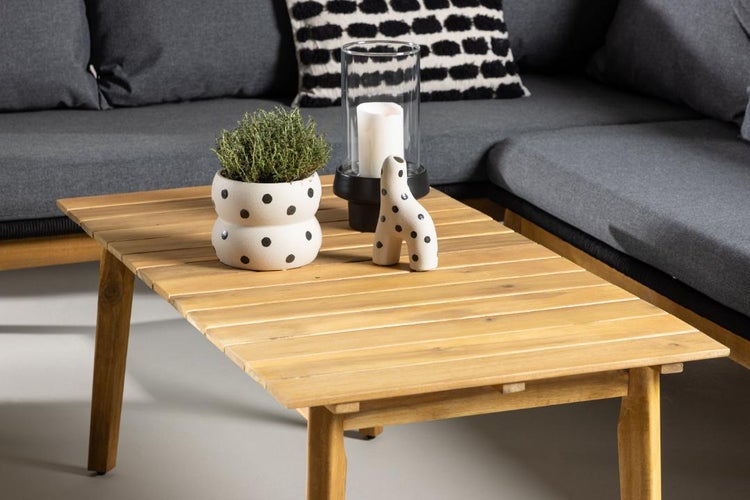 Moderner Loungebereich mit einem Couchtisch aus Holzlatten, dekoriert mit einer Pflanze und einem Kerzenständer vor einem grauen Sofa.