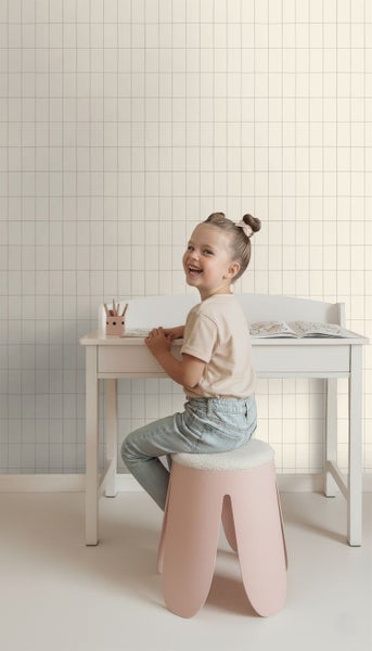 Ein Mädchen sitzt an einem Schreibtisch mit einer gemusterten Tapete im Hintergrund.