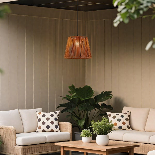 Hell erleuchtete Außen-Lounge mit einer Pendelleuchte aus Holzlamellen, Rattansofas mit Polstern, einem Holztisch und großen Grünpflanzen.