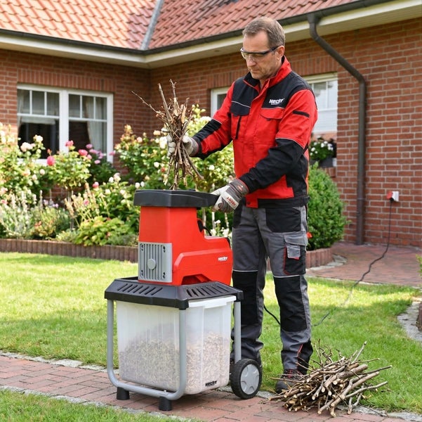 Ein Mann benutzt einen Häcksler der Marke Hecht im Garten, um Äste zu zerkleinern.