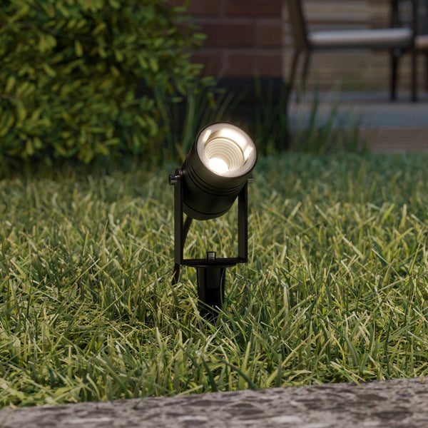 Schwarzer LED-Gartenstrahler mit Erdspieß im Rasen, verstellbarer Lampenkopf mit warmweißem Licht.