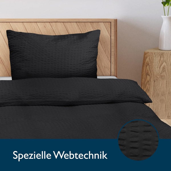 Schwarze Bettwäsche aus Seersucker mit spezieller Webtechnik auf einem Holzbett mit Fischgräten-Kopfteil.
