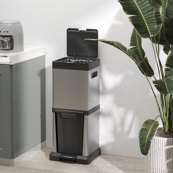 Moderner Abfalleimer aus Edelstahl mit zwei Fächern, oberes Fach mit offenem Deckel, unteres Fach mit Pedal, in einer hellen Küche neben einer Pflanze.