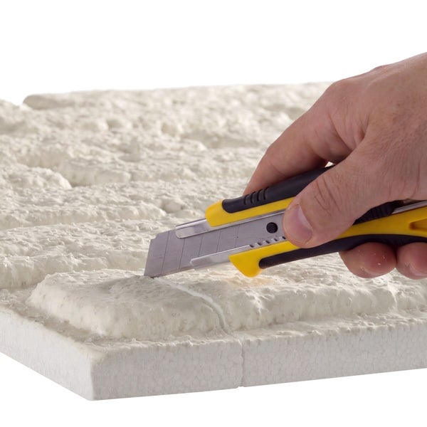 Hand beim Zuschneiden einer Dämmplatte aus Polystyrol mit einem Cuttermesser