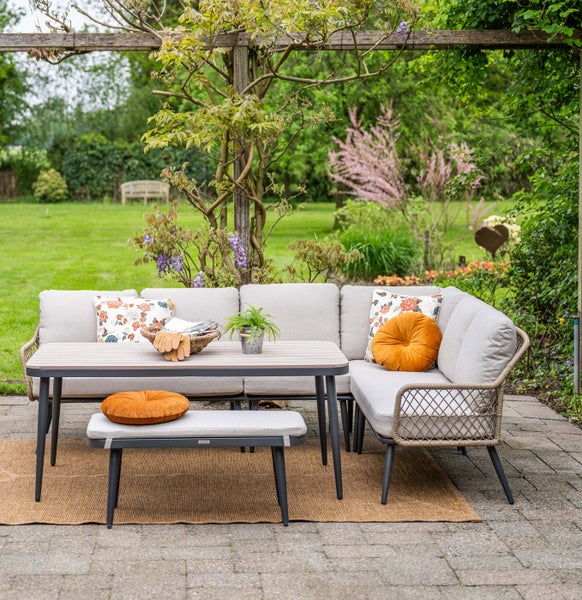 Modernes Garten-Lounge-Set aus Metall und Seilgeflecht mit Ecksofa, Esstisch und Sitzbank auf einer Terrasse in einem hellen, weitläufigen Garten.