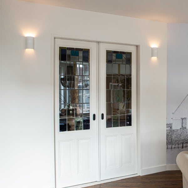 Zwei weiße Flügeltüren mit farbigen Glaseinsätzen und Wandleuchten in einem hellen Raum