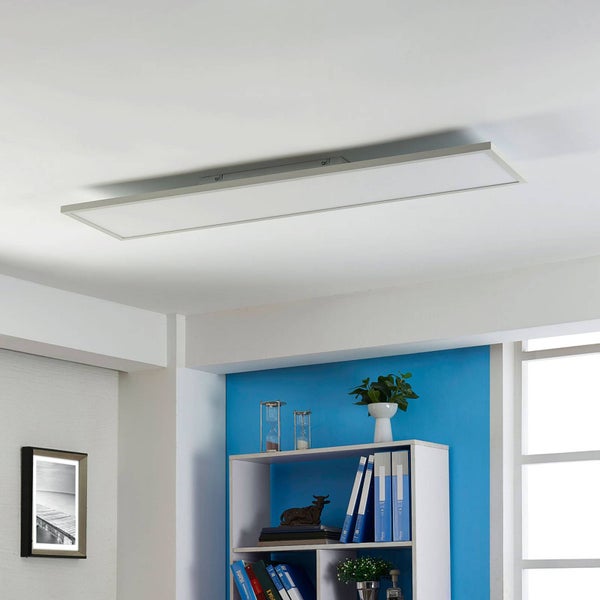 Rechteckiges LED-Panel an einer weißen Zimmerdecke montiert, in einem hellen, modern eingerichteten Raum mit Regal und blauem Wandakzent.