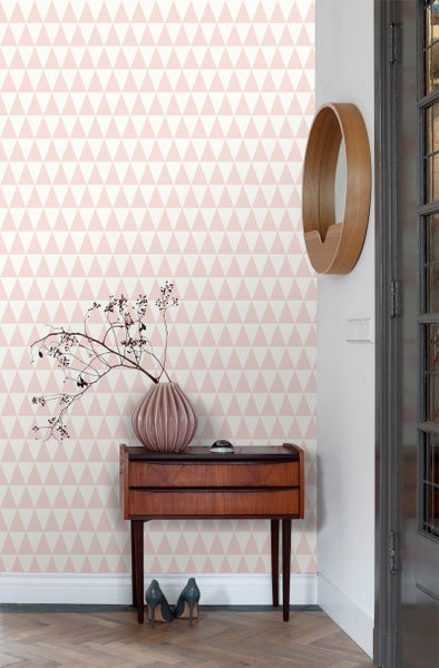Raumansicht mit Tapete mit geometrischem Dreiecksmuster, Holztisch und dekorativen Elementen.