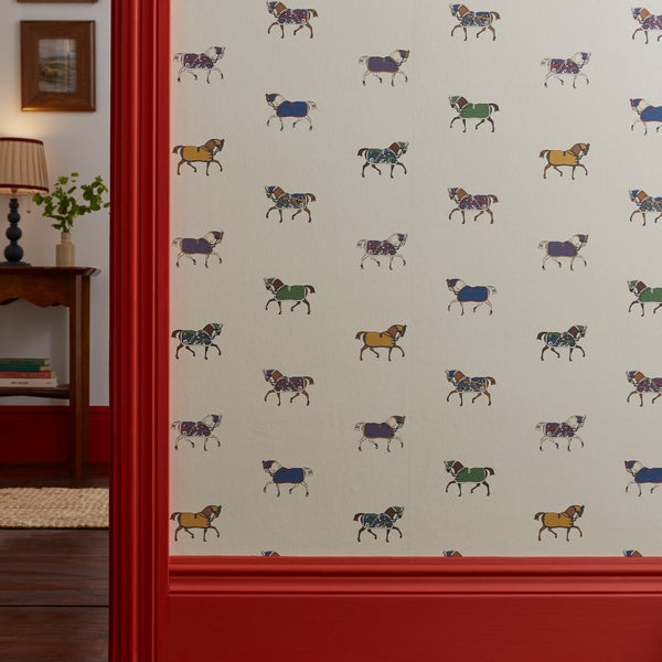 Papiertapete mit Pferdemuster an einer Wand mit roten Holzleisten im historischen Landhausstil.