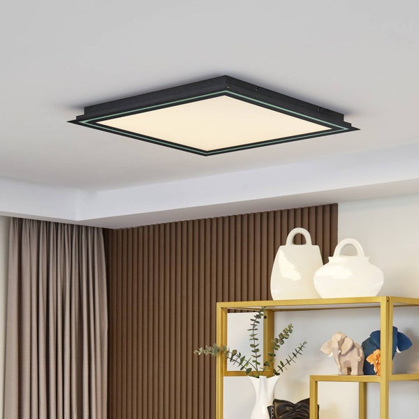 Quadratische LED-Deckenleuchte mit schwarzem Rahmen in einem modernen Wohnraum über einem goldenen Regal und einer Wand aus Holzlamellen.