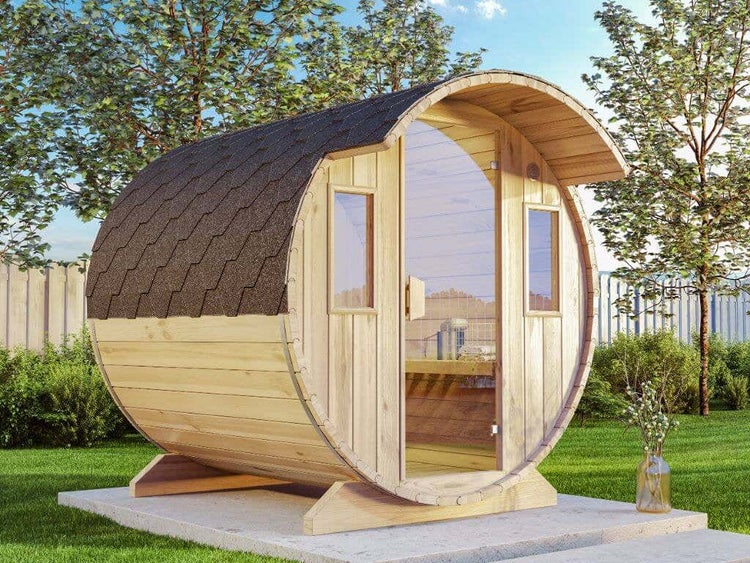 Fasssauna aus Holz mit Glastür, zwei Seitenfenstern und dunklem Schindeldach auf einem Betonsockel im Garten.