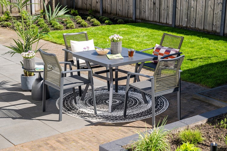 Moderne Gartenmöbelgruppe mit quadratischem Tisch und vier Stühlen mit Seilbespannung auf einem runden Außenteppich auf einer Terrasse.