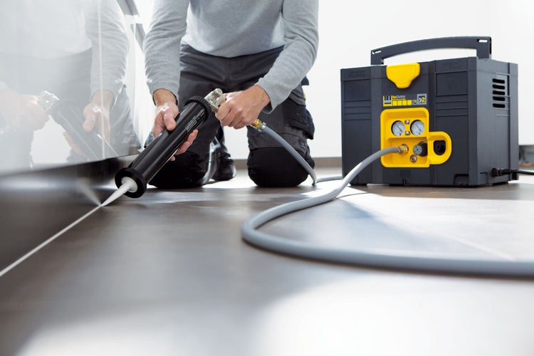 Handwerker verwendet eine Kartuschenpistole mit Kompressor für Silikonfugen