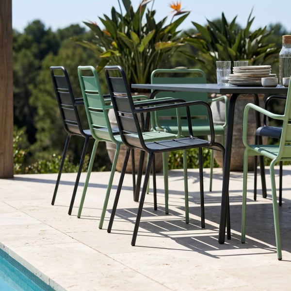 Moderne Garten-Sitzgruppe aus Metall auf einer hellen Steinterrasse am Pool. Gartenstühle mit Armlehnen und Latten-Optik an einem Esstisch.