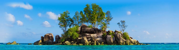 Insel mit Felsen und tropischer Vegetation im Meer unter blauem Himmel