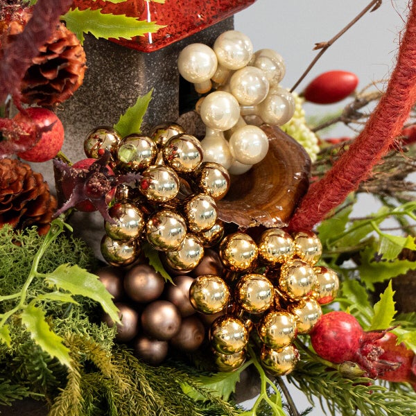 Weihnachtliches Gesteck mit künstlichen Beeren, glänzenden Kugeln, Tannenzapfen und Dekorationselementen in festlicher Optik.